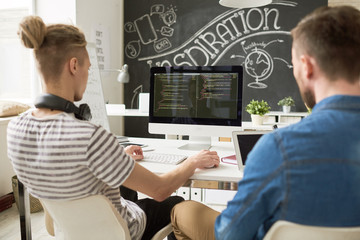 rear view of concentrated coders using computer and analyzing computer program script while working 