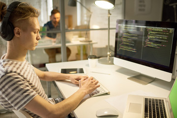 serious hipster computer programmer developing app while composing code and sitting at table with sw