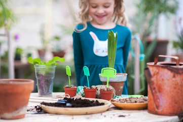 Two sisters are transplanting flowers in pots in the winter garden. Focus on small pots with labels for inscriptions of plants, vegetables