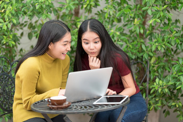 Two students teen girls studying together on line with a laptop in the garden with green tree background.