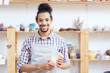 © pressmaster - Portrait of young mixed race man in apron standing in workshop with handmade clay vase and smiling at camera happily