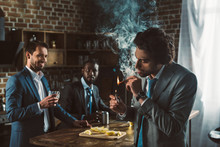 Young Man In Suit Smoking Cigar And Multiethnic Friends Drinking Alcoholic Beverages Behind