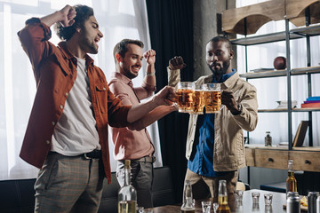 Wall Mural - excited male friends clinking beer glasses while partying together