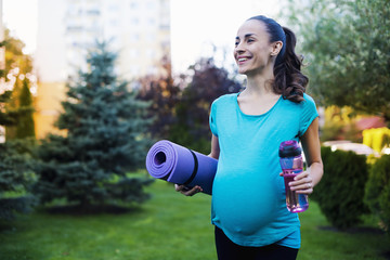 Sports for moms. Beautiful smiling young pregnant woman in sportswear comes with a karemate in hands