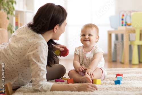Fototapeta Nanny or babysitter looks after kid toddler. Baby girl playing with educational toys in nursery. Child having fun with colorful different toys at home.