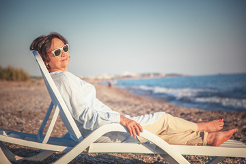 Wall Mural - beautiful elderly woman sitting in a deckchair on the beach and admiring the sunset