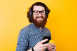 © Vulp - happy smiling bearded man with eyeglasses and headphones using phone and looking at the camera. Coffee to go