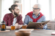 © pressmaster - Two businessmen looking in book and discussing project while drinking tea