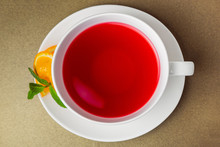 Red Tea Hibiscus In A White Ceramic Cup And Orange Slice With Mint Like A Flower On A Mug. Net Food, Weight Loss, The Concept Of Vegetarian Food