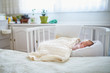 Newborn baby having a nap in co-sleeper crib attached to parents' bed