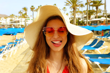 Portrait of beautiful blonde woman with straw hat and sunglasses having fun at beach. Funny dreaming girl in her summer holidays.