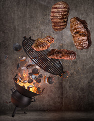 Wall Mural - Kettle grill with hot briquettes, cast iron grate and tasty beef steaks flying in the air. High resolution image.