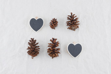 Two tiny heart shape blackboards with pinecones on muslin fabric background