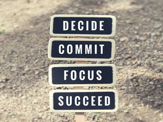 Words ‘decide, commit, focus, succeed’ written on a black signboards.
