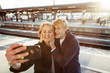 © Maskot - Cheerful young couple taking selfie through mobile phone on railroad station platform