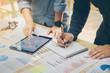 © Pcess609 - Startup Concept.Young businessman holding pen Writing a summary report on a notebook and A friend pointing on tablet to explain the work plan at home office.