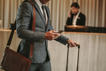 businessman in hotel lobby with phone and luggage