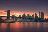 Fototapeta Miasta - Famous Brooklyn Bridge in New York City with financial district - downtown Manhattan in background. Sightseeing boat on the East River and beautiful sunset over Jane's Carousel.