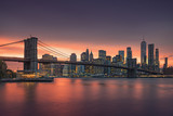 Fototapeta Most - Famous Brooklyn Bridge in New York City with financial district - downtown Manhattan in background. Sightseeing boat on the East River and beautiful sunset over Jane's Carousel.