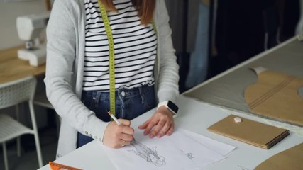 Wall Mural - Tilt-up shot of creative clothing designer concentrated on drawing sketch of women's garment on piece of paper with pencil. Creating fashionable clothes concept.