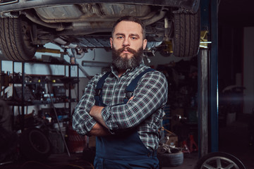 Two bearded brutal mechanics repair a car on a lift in the garage. 