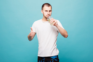 Handsome young man drinking bottle with summer drink, thumbs up and looking at camera isolated on green