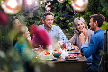 Group of friends gathered around a table in a garden on a summer evening to share a meal and have a good time together