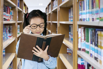 Wall Mural - Little girl reading a textbook in the library