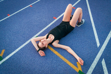 Wall Mural - Top view of athletic woman lying on running track and resting after training