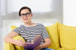 © LIGHTFIELD STUDIOS - smiling teen boy sitting with violet book on yellow sofa at home