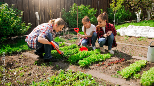 Fotomural Happy young woman with daughters planting seeds in garden