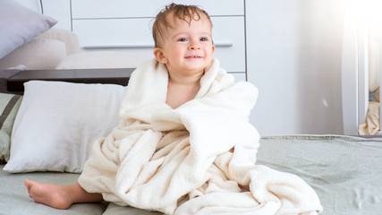 Wall Mural - Portrait of cute smiling toddler boy sitting under towel after bath