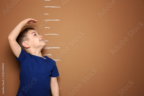 Fotografía Little boy measuring his height on color background