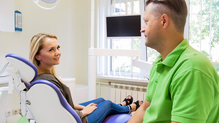 Wall Mural - Portrait of beautiful blonde woman talking to male dentist in clinic