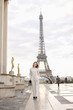 Stylish fashionable woman in white overalls walking on Trocadero square near gilded statues and Eiffel Tower in Paris. Concept of trip to France and European landmarks.