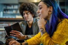 Tattooed Modern Woman Using Laptop, Man Taking Notes In Background.Group Of Multiethnic People Having Business Team Meeting In Restaurant Lounge.Teamwork,corporate,diversity And Social Concepts.