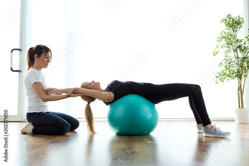 Fotografía Physiotherapist helping patient to do exercise on fitness ball in physio room