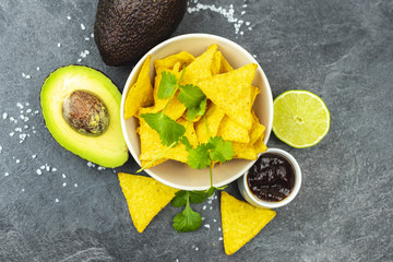 Tortilla chips and lime with salt and avocado on the black wooden table. 