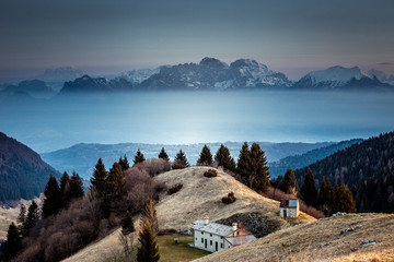 Sunrise on a small hut with in the background the Mount Schiara dolomite peaks that emerge from the mists, Pian de le Femene, Veneto, Italy