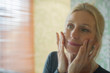 © PhotoAlto - Mature woman looking at her reflection in mirror with hands on cheeks