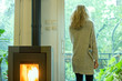 © PhotoAlto - Woman standing in living room, looking out window