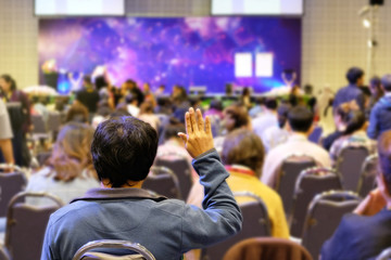 Audience raising hand up and listening speaker who standing in front of the room at the conference hall, Business and Entrepreneurship concept.