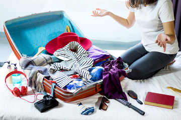 Travel and vacation concept, happiness woman packing stuff and a lot of clothes into suitcase on bed prepare for her travel and journey trip