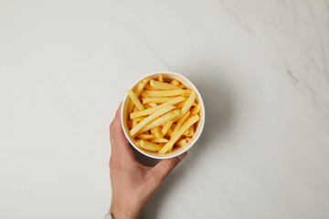 Wall Mural - cropped shot of man holding bowl of delicious french fries on white