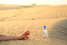 Hand Try To Catch The Bottle Of Water On Sand Desert In Hot Temperature. Concept Of To Die Of Thirst.
