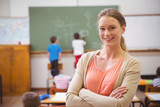 Fototapeta  - Pretty teacher smiling at camera at back of classroom