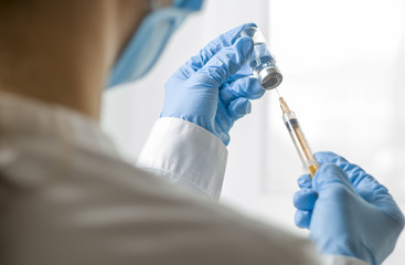 Wall Mural - A syringe and a bottle with an injection solution, against the background of a medical worker. The doctor is holding a syringe with vaccination. Liquid medication or drug.