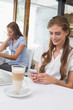 © WavebreakmediaMicro - Smiling woman using mobile phone in coffee shop