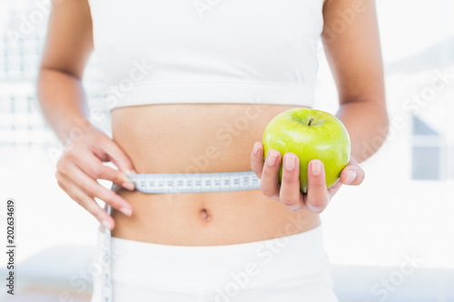 Fotografía Mid section of woman measuring waist as she holds apple