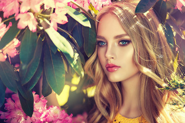  Beautiful spring model girl in flowers in summer blossom park. Woman in a blooming garden . Fashion, Cosmetics & Perfumes . Curly blonde hair 